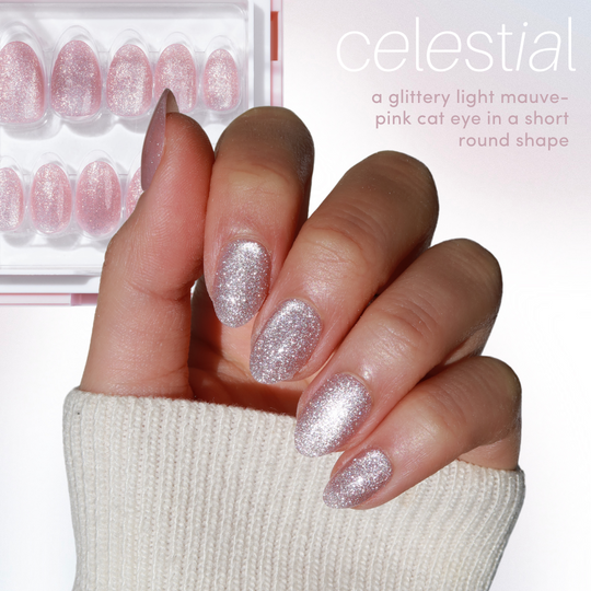A hand with short, round nails painted in glittery mauve-pink cat eye polish peeks from a sweater sleeve. Nearby, a set of Glowie By Her's 11:11 Collection Vol. 1 (20% off) false nails reflects chrome nail styles, under the text "celestial.