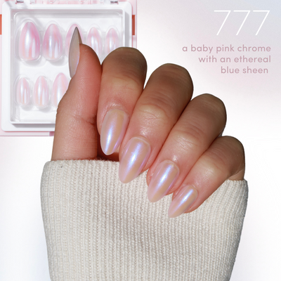 A hand adorned with stunning, glossy baby pink chrome nails exhibits an enchanting blue sheen, ideal for infusing a magical touch into your style. Behind it sits a box of comparable false nails, just in time for the Black Friday Sale. The text reads "11:11 - Full Collection from Glowie By Her featuring a baby pink chrome with an ethereal blue sheen (35% Off).