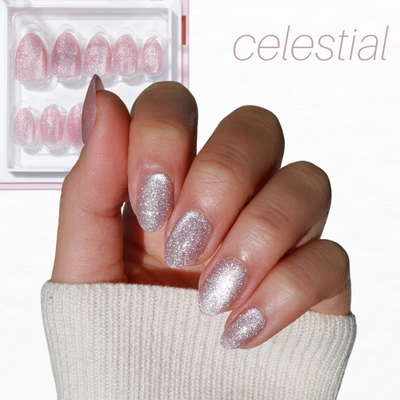 A hand with sparkly pink nails delicately holds a transparent box of Cosmic Dreams from Glowie By Her, featuring extra nails. The background is white, and the word "celestial" is elegantly written in pink text at the top right.