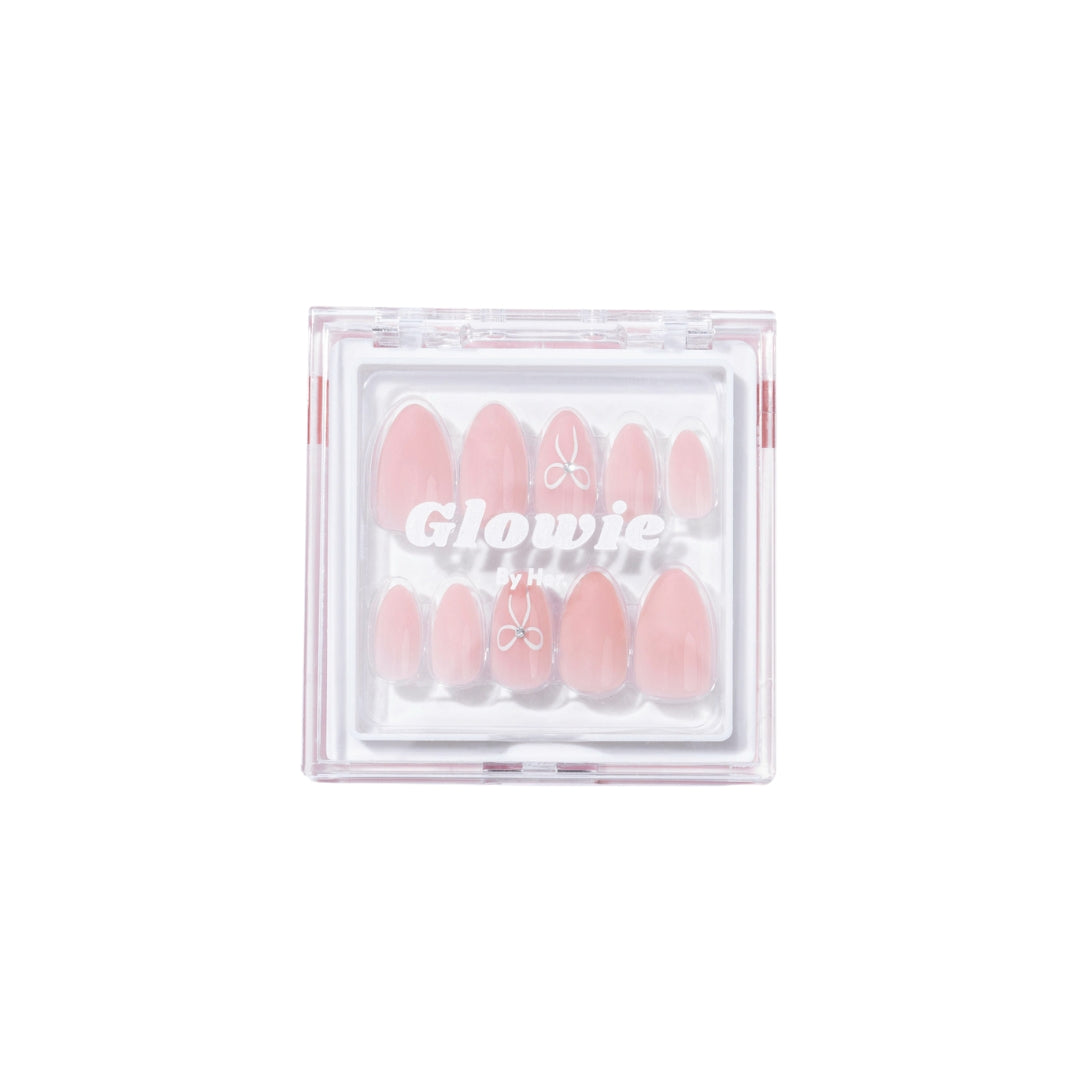 A clear plastic box from Glowie By Her contains a set of Cutie Press-On Nails in baby pink, each adorned with a small white butterfly design. The almond-shaped nails are neatly arranged inside the box, with the brand name "Glowie By Her" printed on the front of the packaging.