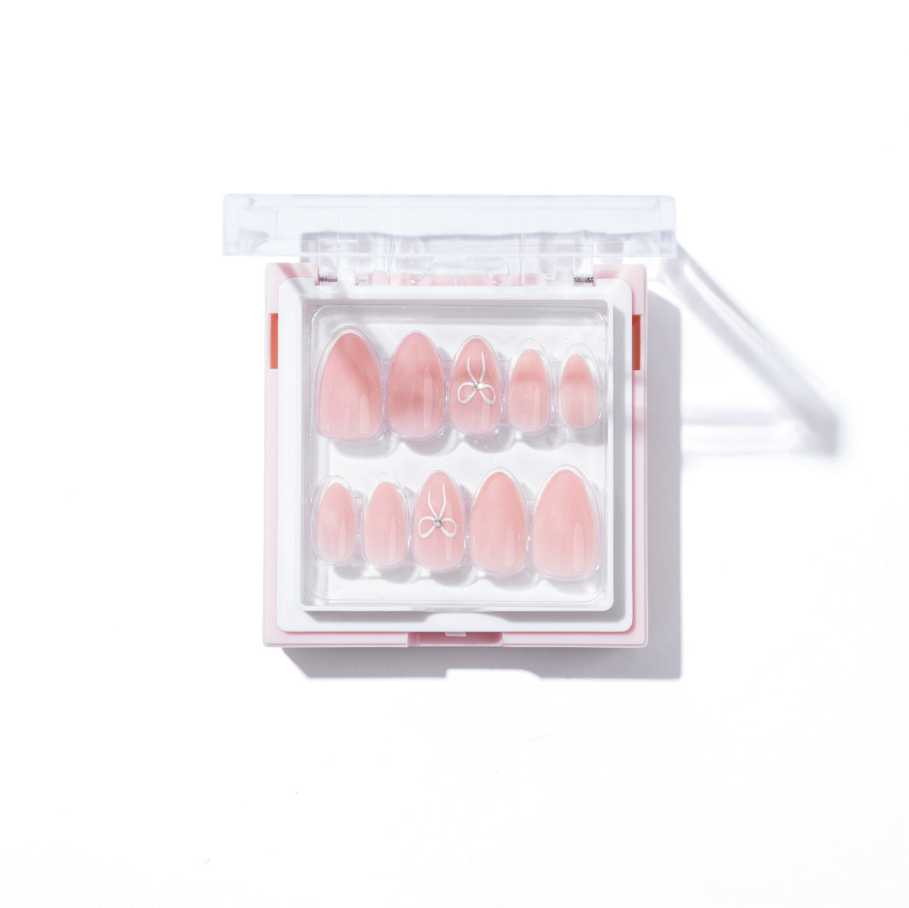 The Cutie Press-On Nails by Glowie By Her are a set of customisable baby pink nails in various almond shapes, neatly arranged in a transparent plastic case. Some nails feature small, delicate white bow designs. The case has a clear lid and is placed on a clean white surface.