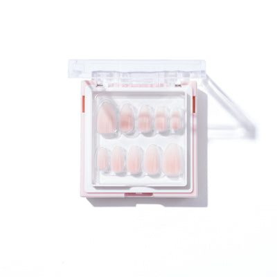 An open plastic case displays a set of Daydream Press-On Nails (Short) by Glowie By Her, arranged in two rows. Designed to fit various fingernail shapes, the short almond-style nails come in different sizes. The transparent, rectangular case has a white backing and clear lid, showcasing the oval nails in a neutral color.