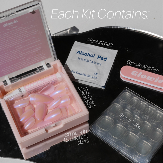 A pink nail kit from Glowie By Her's Valentine's Day Collection (20% Off) is elegantly shown on a marble surface. It includes a case with 30 iridescent pink nails, an alcohol pad, nail file, glue, cuticle stick, sticky tabs, and 15 vegan & cruelty-free sizes.