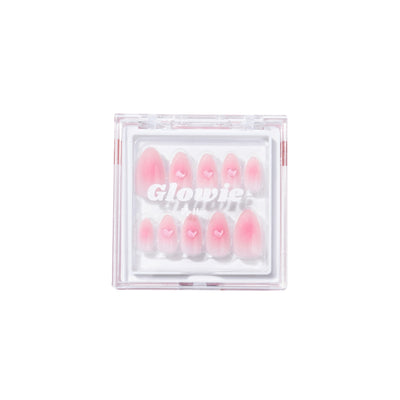 A square, transparent plastic case containing the "Made You Blush Press-On Nails" by Glowie By Her is shown. The salon-quality nails feature a blush nail base with tiny 3D gel heart accents, and some have a gradient effect. The brand name "Glowie By Her" is printed on the case lid.