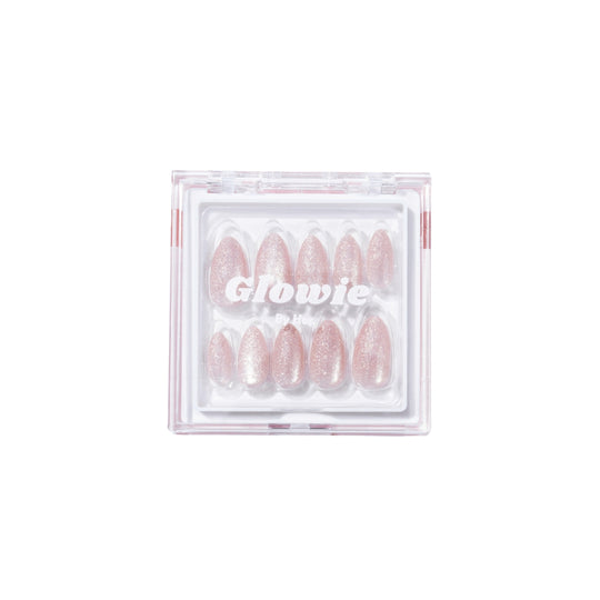 A clear plastic package containing a set of glittery pink almond-shaped press-on nails, offering salon-quality allure, is neatly arranged in two symmetrical rows. The product name "Make a Wish" by the brand "Glowie By Her" is printed in white on the front of the package.