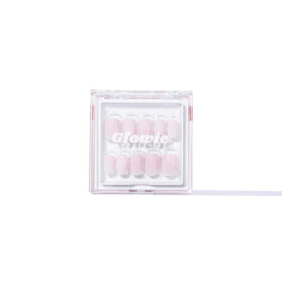 A transparent plastic box showcasing the Pillowtalk Press-On Nails set, featuring salon-quality light pink nails, is arranged neatly inside. The brand name "Glowie By Her" is prominently displayed on the top of the packaging. This elegant nail kit sits on a plain white background, emphasizing its chic and professional appeal.