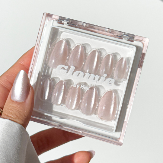 A hand displays a transparent plastic box of Glowie By Her's salon-quality, pearlescent pink press-on nails named ASAP. The person's thumbnail is painted to match these chic ASAP nails in the box.