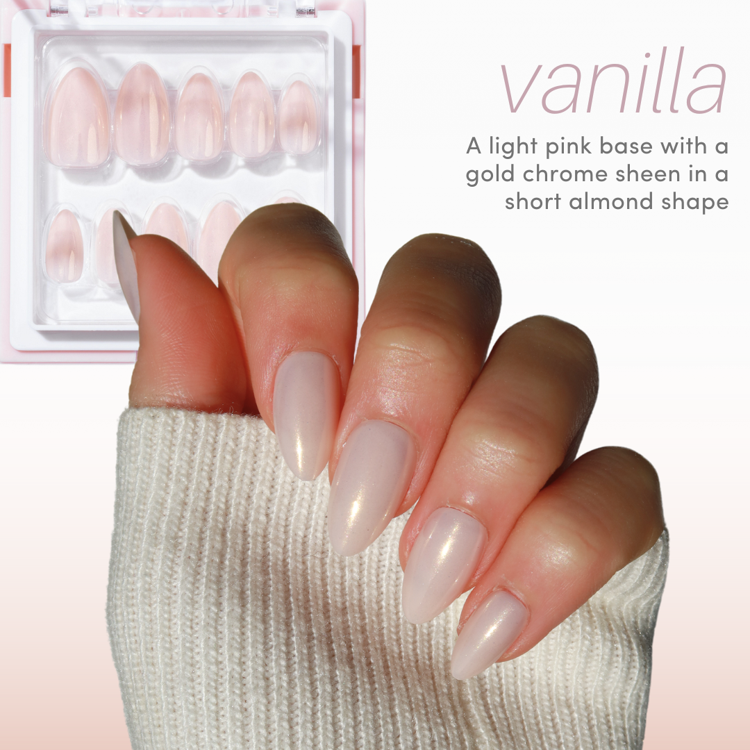 A hand features almond-shaped nails in light pink with a gold chrome sheen from Glowie By Her's Chrome Crush Collection (10% Off), paired with a cream sweater sleeve. A "vanilla" nail package sits nearby, ideal for reusable Glowie cases.
.